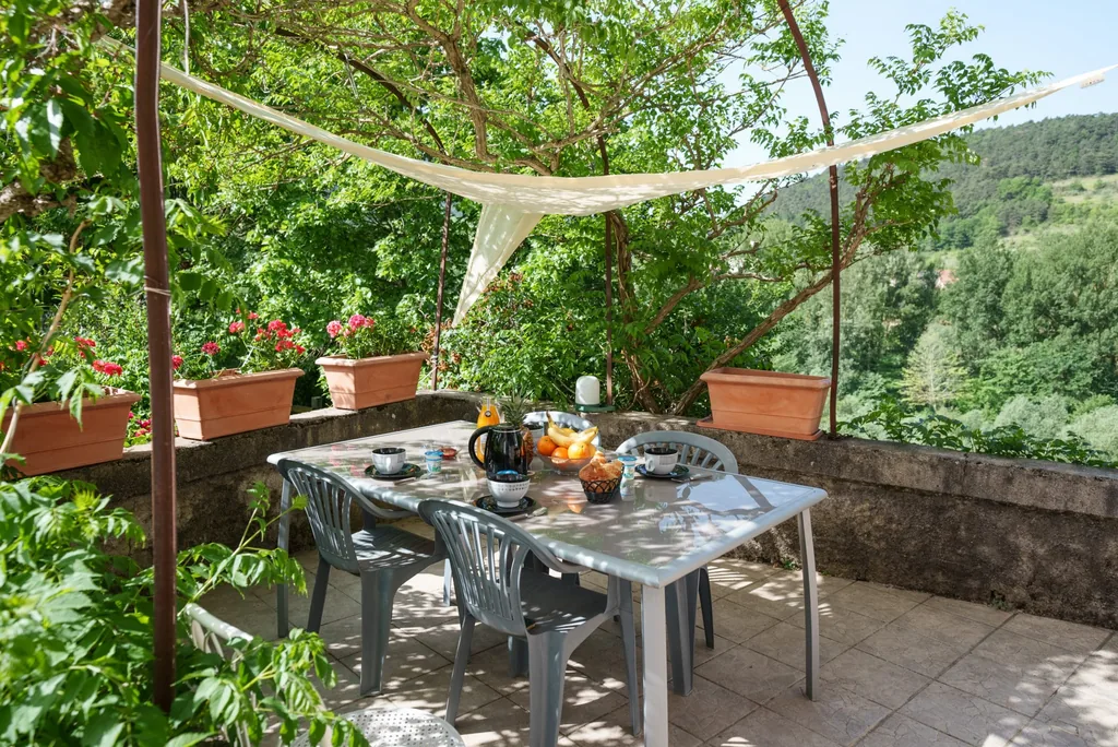 Grande terrasse ombragée du gîte Au bord du Tarn, table dressée face à la vallée à La Cresse en Aveyron
